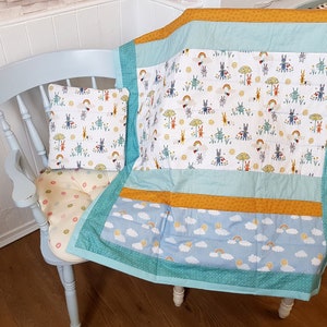 May include: A blue chair with a white and yellow patterned cushion. A white and blue baby quilt with a bunny and rainbow pattern is draped over the chair.