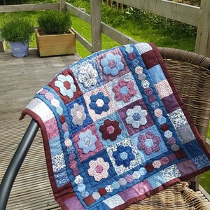 May include: A blue and purple patchwork quilt with a floral design. The quilt is made of squares and hexagons, and it is sitting on a wicker chair.