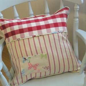 Puede incluir: Una almohada de cuadros rojos y blancos con un panel de tela a rayas y un bolsillo de parche floral. La almohada está sentada en una silla azul claro.