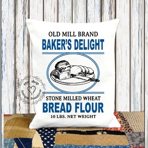 Puede incluir: Almohada blanca con una ilustraci&oacute;n de estilo vintage de pan en un plato. El texto dice "Old Mill Brand Baker's Delight Stone Milled Wheat Bread Flour 10 lbs. Net Weight".