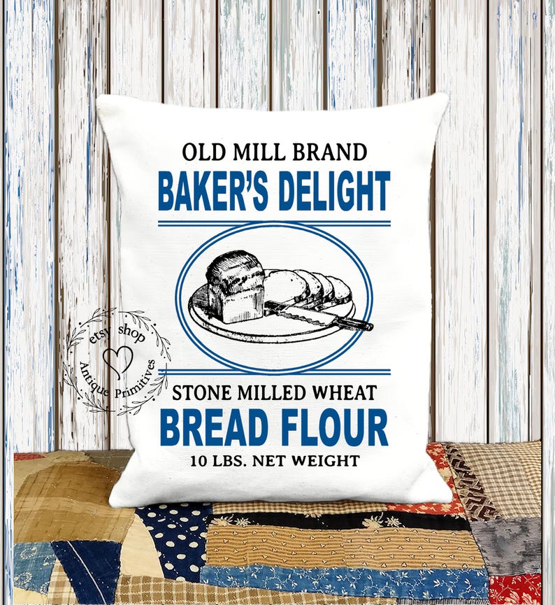 Puede incluir: Almohada blanca con una ilustraci&oacute;n de estilo vintage de pan en un plato. El texto dice "Old Mill Brand Baker's Delight Stone Milled Wheat Bread Flour 10 lbs. Net Weight".