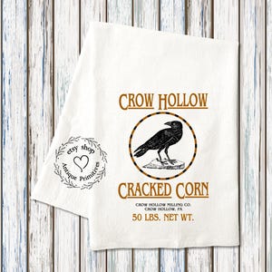 K&ouml;nnte beinhalten: Ein wei&szlig;es Geschirrtuch mit einer schwarzen Kr&auml;henillustration und dem Text "CROW HOLLOW CRACKED CORN CROW HOLLOW MILLING CO. CROW HOLLOW, PA 50 LBS. NET WT."