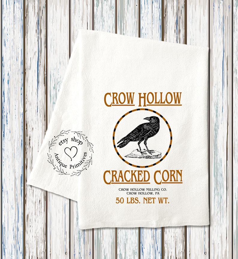 K&ouml;nnte beinhalten: Ein wei&szlig;es Geschirrtuch mit einer schwarzen Kr&auml;henillustration und dem Text "CROW HOLLOW CRACKED CORN CROW HOLLOW MILLING CO. CROW HOLLOW, PA 50 LBS. NET WT."