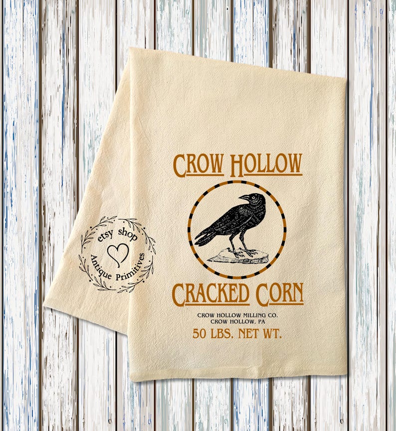 K&ouml;nnte beinhalten: Ein beigefarbenes K&uuml;chentuch mit einer schwarzen Kr&auml;henillustration und dem Text "CROW HOLLOW CRACKED CORN CROW HOLLOW MILLING CO. CROW HOLLOW, PA 50 LBS. NET WT."