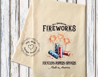 May include: A beige kitchen towel with a red, white, and blue fireworks design. The text "ALL AMERICAN FIREWORKS" is printed in black. The text "FOUNTAINS-POPPERS-SPINNERS Made in America" is printed in black below the fireworks.