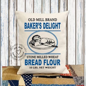 Puede incluir: Una almohada blanca con una ilustraci&oacute;n de estilo vintage de pan en un plato. El texto dice "Old Mill Brand Baker's Delight Stone Milled Wheat Bread Flour 10 lbs. Net Weight".