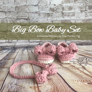 May include: A pink crocheted baby headband with a bow and a pair of pink crocheted baby booties with bows. The booties have a white trim. The text "Big Bow Baby Set" and "A Crochet Pattern by One Paisley Pig" is visible in the image.