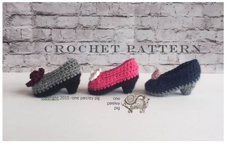 May include: Three crochet shoe ornaments with heels, featuring a gray shoe with a dark red flower, a pink shoe with a white flower, and a navy blue shoe with a light pink flower. The text CROCHET PATTERN, copyright 2015 -one paisley pig, and one paisley pig are visible.