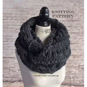 Puede incluir: Una bufanda de cuello de tortuga de punto gris oscuro con un patrón de punto de cable. La bufanda se muestra en un maniquí contra una pared de ladrillo blanco. El texto "Knitting Pattern" se muestra sobre la bufanda y "copyright © 2015 - one paisley pig" se muestra debajo de la bufanda.