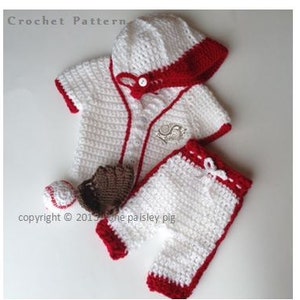 May include: Crochet baseball outfit for a baby, featuring a white and red baseball jersey, trousers, hat, and a brown glove and ball.