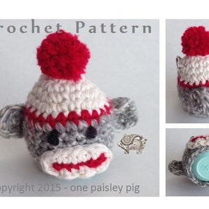 Könnte beinhalten: Gehäkeltes Affenspielzeug mit roter Bommelmütze. Der Affe ist grau mit weißen und roten Details. Das Spielzeug ist so konzipiert, dass es auf einen kleinen runden Behälter passt, wie z. B. einen EOS Lippenbalsam.