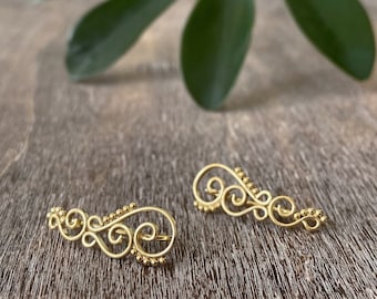 May include: A pair of gold ear cuffs with a delicate, ornate design. The cuffs are made of thin wire and feature small, round beads.