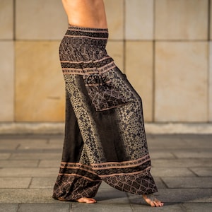 Könnte beinhalten: Schwarz-braune Haremshose mit Muster und weitem Bein. Die Hose hat ein detailliertes geometrisches Muster mit rosafarbenen Zierleisten an den Taschen und Knöcheln. Sie hat einen elastischen Bund.