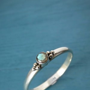 Könnte beinhalten: Ein silberner Ring mit einem hellblauen Edelstein und kleinen silbernen Perlen auf der Ringschiene.