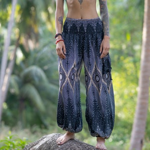 Könnte beinhalten: Schwarz-weiße gemusterte Hose mit goldenem Design. Die Hose ist locker geschnitten und hat eine weite Beinweite.