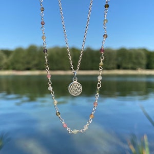 May include: A silver necklace with a flower of life pendant and a second necklace with small, colorful beads.