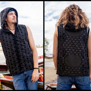 Può includere: Gilet nero senza maniche con cappuccio e motivo geometrico. Il gilet ha una cerniera a tutta lunghezza e un cappuccio. Il motivo è un disegno ripetuto di forme interconnesse. Il gilet è indossato sopra una camicia scura e jeans blu.