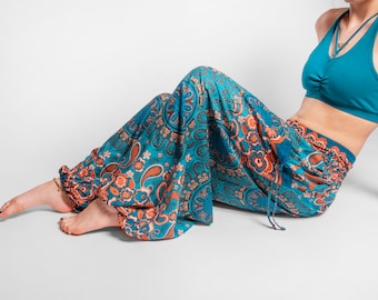 May include: A person wearing teal blue and orange patterned pants with a teal blue sports bra. The pants have a drawstring waist and are gathered at the ankles.