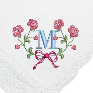 May include: White cotton handkerchief with a lace border. The handkerchief features an embroidered design of pink roses and a blue letter "M" with a pink bow.
