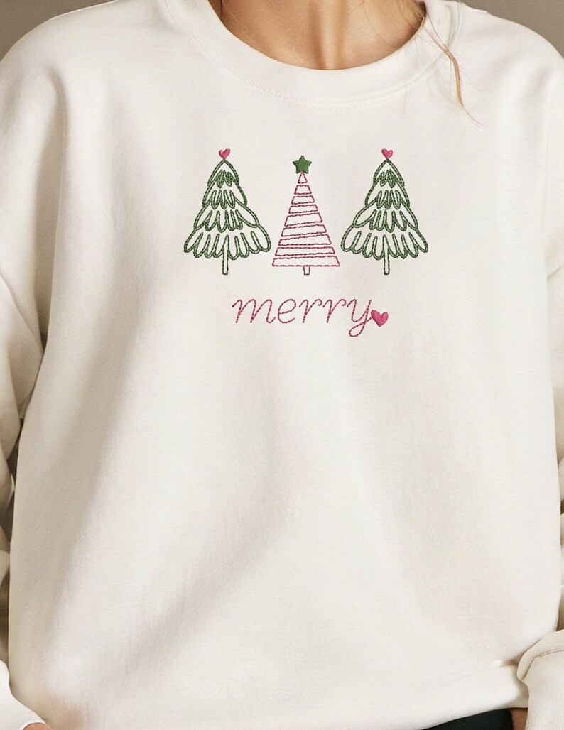 May include: White sweatshirt with a green, pink, and red embroidered design of three Christmas trees and the word "merry" with a pink heart.