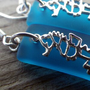 May include: A pair of silver seahorse earrings with blue glass teardrop-shaped dangles. The earrings have a simple hook closure.