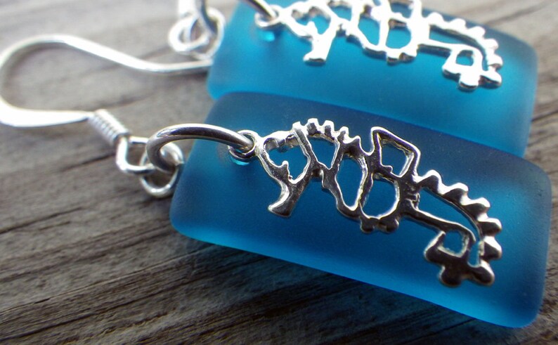 May include: A pair of silver seahorse earrings with blue glass teardrop-shaped dangles. The earrings have a simple hook closure.