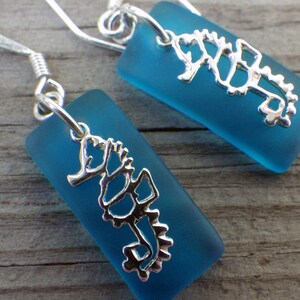 May include: A pair of silver earrings with a blue glass seahorse charm. The seahorse is a delicate, detailed design.