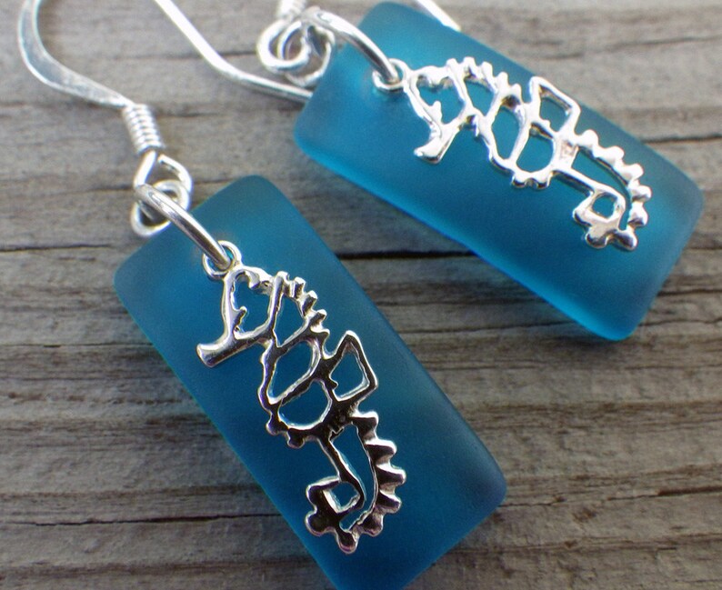 May include: A pair of silver earrings with a blue glass seahorse charm. The seahorse is a delicate, detailed design.