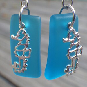 May include: A pair of blue glass earrings with silver seahorse charms. The earrings are rectangular in shape and have a frosted finish.