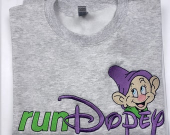 May include: Gray sweatshirt with a purple and green embroidered design featuring the Disney logo and the word "run" followed by the character Dopey from the movie Snow White and the Seven Dwarfs. The design also includes the text "Dopey" in purple.