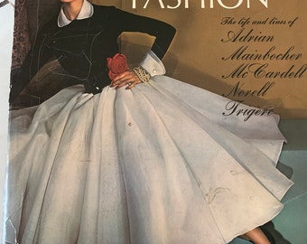 May include: Book cover featuring a black and white photo of a woman wearing a white dress and a black top. The book title is "American Fashion" and lists the names of designers: Adrian, Mainbocher, Mc Cardell, Norell, and Trigere. The book is by Sarah Tomerlin Lee and published by The Fashion Institute of Technology.