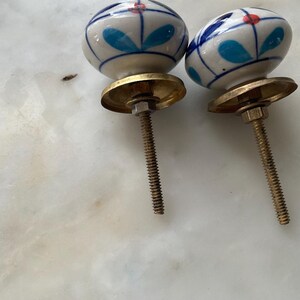 Puede incluir: Dos pomos de caj&oacute;n de cer&aacute;mica con un dise&ntilde;o floral azul y blanco y detalles rojos. Los pomos tienen una base de lat&oacute;n y un tornillo.