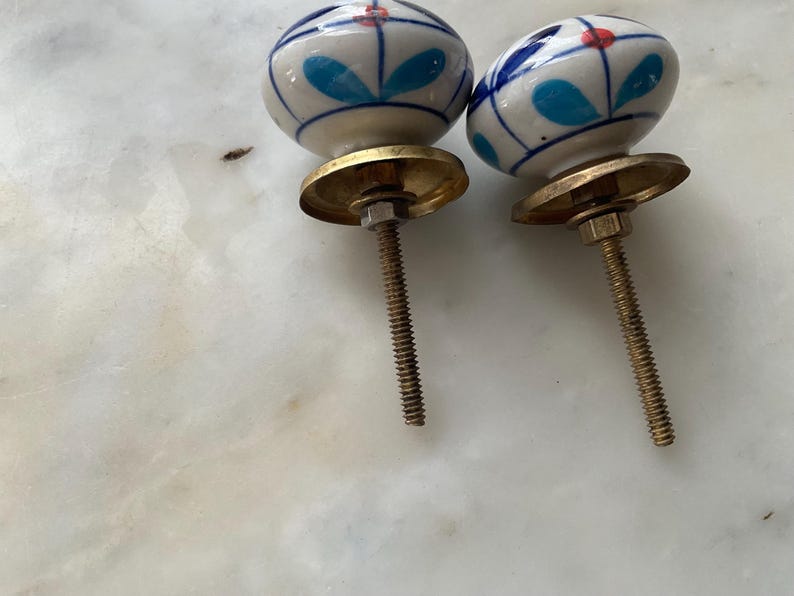 Puede incluir: Dos pomos de caj&oacute;n de cer&aacute;mica con un dise&ntilde;o floral azul y blanco y detalles rojos. Los pomos tienen una base de lat&oacute;n y un tornillo.