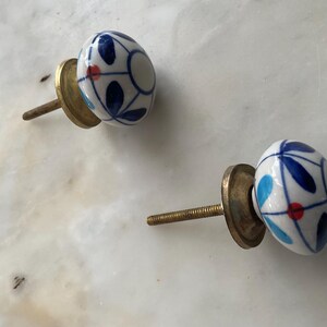 Puede incluir: Dos pomos de caj&oacute;n de cer&aacute;mica con base blanca y dise&ntilde;os florales azules y rojos. Los pomos tienen un tornillo y una base de lat&oacute;n.