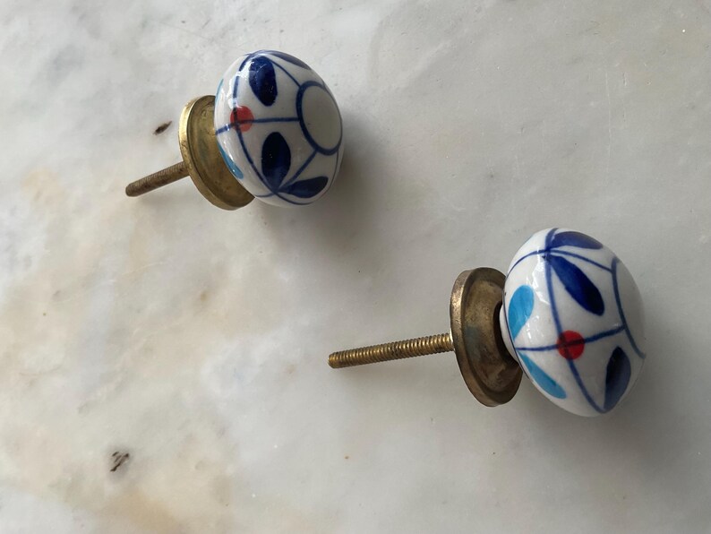 Puede incluir: Dos pomos de caj&oacute;n de cer&aacute;mica con base blanca y dise&ntilde;os florales azules y rojos. Los pomos tienen un tornillo y una base de lat&oacute;n.