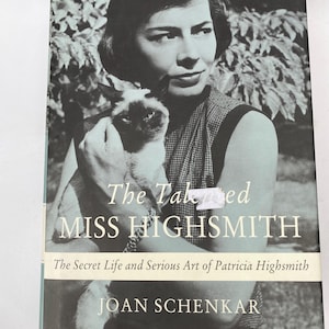 May include: Black and white book cover featuring a woman holding a Siamese cat. The title reads "The Talented Miss Highsmith" by Joan Schenkar. The subtitle is "The Secret Life and Serious Art of Patricia Highsmith."