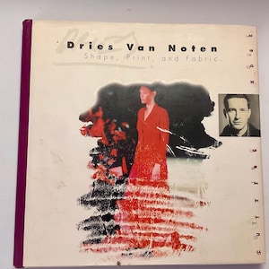 May include: The book "Dries Van Noten: Shape, Print, and Fabric" displays a woman in a red coat and a portrait of a man. The cover is white with red and black abstract art and a purple spine.