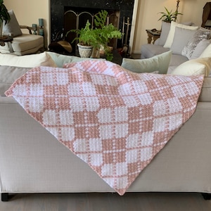 May include: A pink and white crocheted throw blanket with a checkered pattern is draped over a light gray couch.