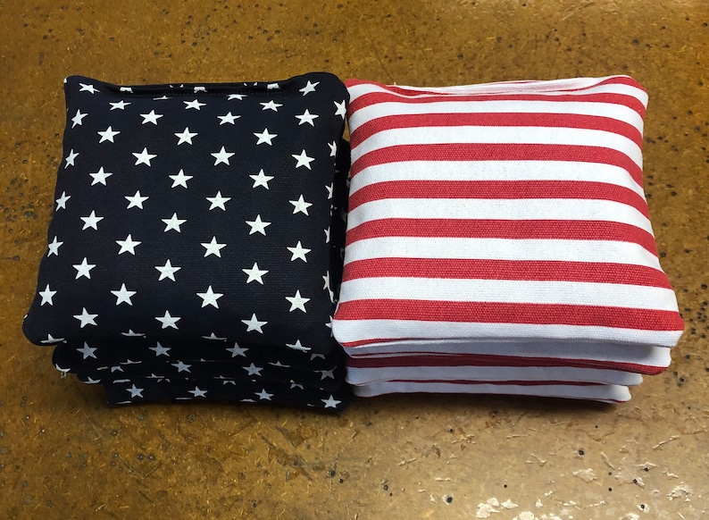 May include: Two cornhole bean bags. One bag is navy blue with white stars, and the other is red and white striped. The bags are stacked on top of each other.