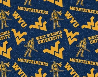 May include: A dark blue fabric featuring a repeating pattern of yellow West Virginia University Mountaineers logos, the text West Virginia University, and the Mountaineer mascot holding a rifle, with a ruler visible at the bottom edge.