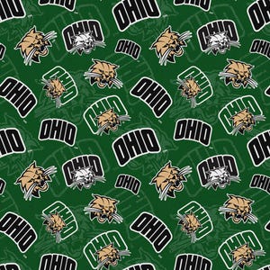 May include: A dark green fabric featuring a repeating pattern of the Ohio University bobcat mascot head in tan and white, alongside the word OHIO in bold black letters with white outlines, arranged in a dense, multi-directional layout.