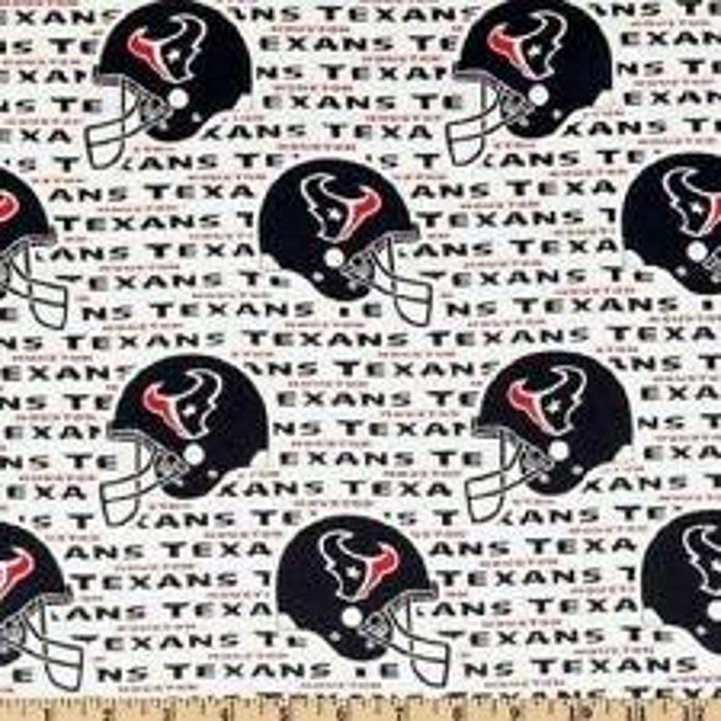 May include: A white fabric featuring a repeating pattern of dark blue Houston Texans football helmets with red and white logos, interspersed with the repeated black text "HOUSTON TEXANS" printed in a bold, sans-serif font across the entire surface.