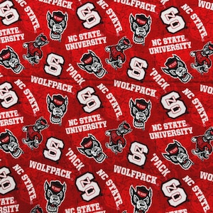 May include: Red fabric with a repeating pattern of white "S" logos, the words "NC State University" and "Wolfpack", and a cartoon wolf mascot. The design is a collegiate theme.