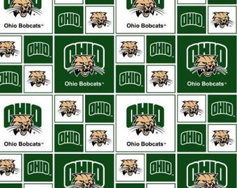 May include: A repeating pattern fabric featuring the Ohio Bobcats logo, which consists of a tan bobcat head with whiskers and the word OHIO in green block letters. The design alternates between white and dark green square backgrounds.