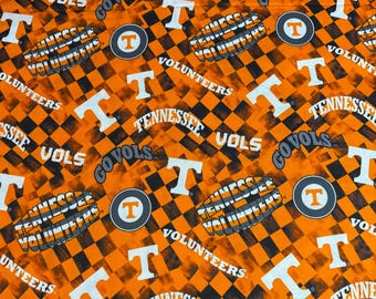 May include: Fabric featuring a repeating checkerboard pattern in orange and black. The design includes the white letter T, the text Tennessee Volunteers in white, and circular logos containing a white T on an orange background with a gray border.