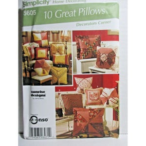 Könnte beinhalten: Eine Simplicity 5605 Schnittmusterhülle mit dem Titel 10 Great Pillows Decorators Corner von Sunrise Designs. Die Vorderseite zeigt Fotografien verschiedener dekorativer Zierkissen in roten, goldenen und gemusterten Stoffen mit Quasten.
