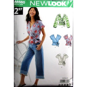 May include: A New Look sewing pattern envelope A6560 featuring a wrap-style top with a V-neckline, short sleeves, and a tie waist. The pattern displays three variations of the top in floral and solid prints, alongside a model wearing the wrap top.