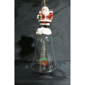 Puede incluir: Adorno navideño en forma de campana de cristal transparente con una figura de Papá Noel en la parte superior. La figura de Papá Noel lleva un traje rojo y sostiene una bolsa verde. La campana tiene un lazo dorado para colgar.
