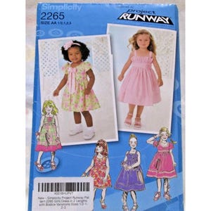 Puede incluir: Patrón de costura Simplicity 2265 para vestidos de niña. El patrón presenta varios diseños de vestidos, incluyendo un vestido rosa y un vestido floral. El paquete incluye tallas AA 1/2, 1, 2 y 3. Inspirado por Project Runway.