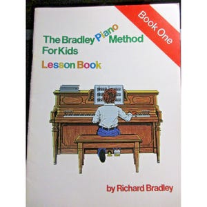 Puede incluir: El libro de lecciones del método Bradley Piano para niños, Libro uno, por Richard Bradley. La portada presenta una ilustración de un niño tocando el piano.